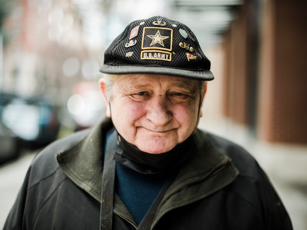A white male senior citizen wearing a US army baseball cap. 