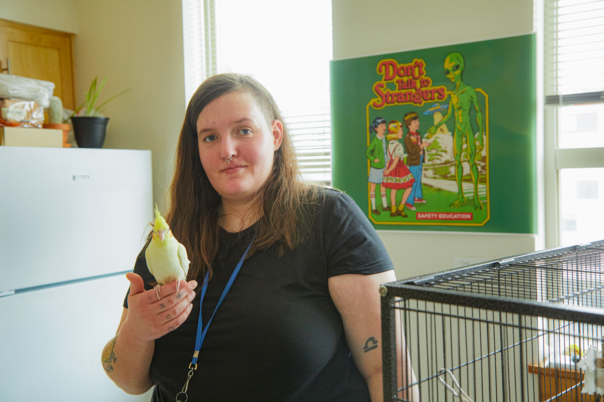 Woman in black shirt in apartment holding cockatiel beside cage