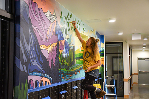 Artist at work painting on mural in the entryway of a residential building