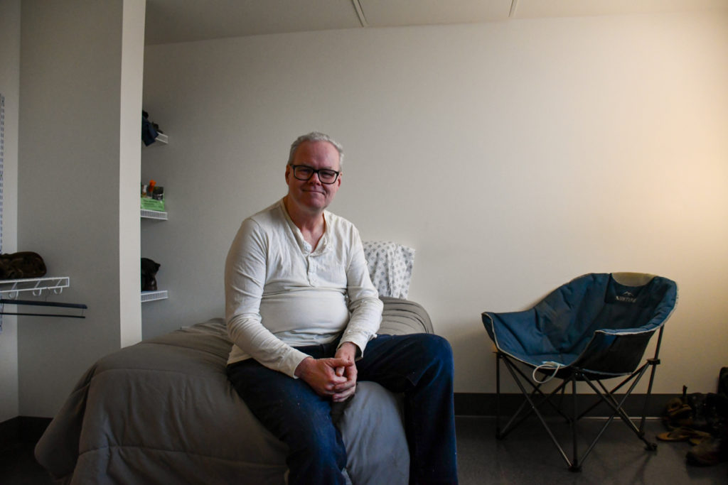 A man sits on his bed in a studio apartment