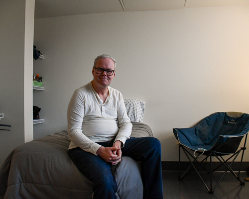 A man sits on a bed in a studio apartment